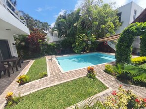 A swimming pool surrounded by a well-maintained garden with a variety of plants and a small grassy area. - Azul Mar Apartment 2 (Puerto Morelos)