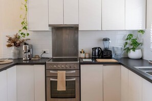 A modern kitchen with stainless steel appliances, white cabinetry, and a central island. - Cosy & Central Apartment: Fast Wifi, Walk to beach (Scarborough)