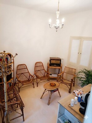 A room with wicker furniture, a table, a bookshelf, and a radio. - Guest House San Giorgio – In the Heart of Caltagirone with a Panoramic Terrace (Caltagirone)