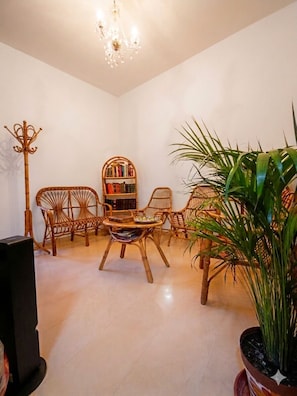 Ein Raum mit einer Chandelüster, Korbmöbeln, einem Bücherregal und einem Blumentopf.