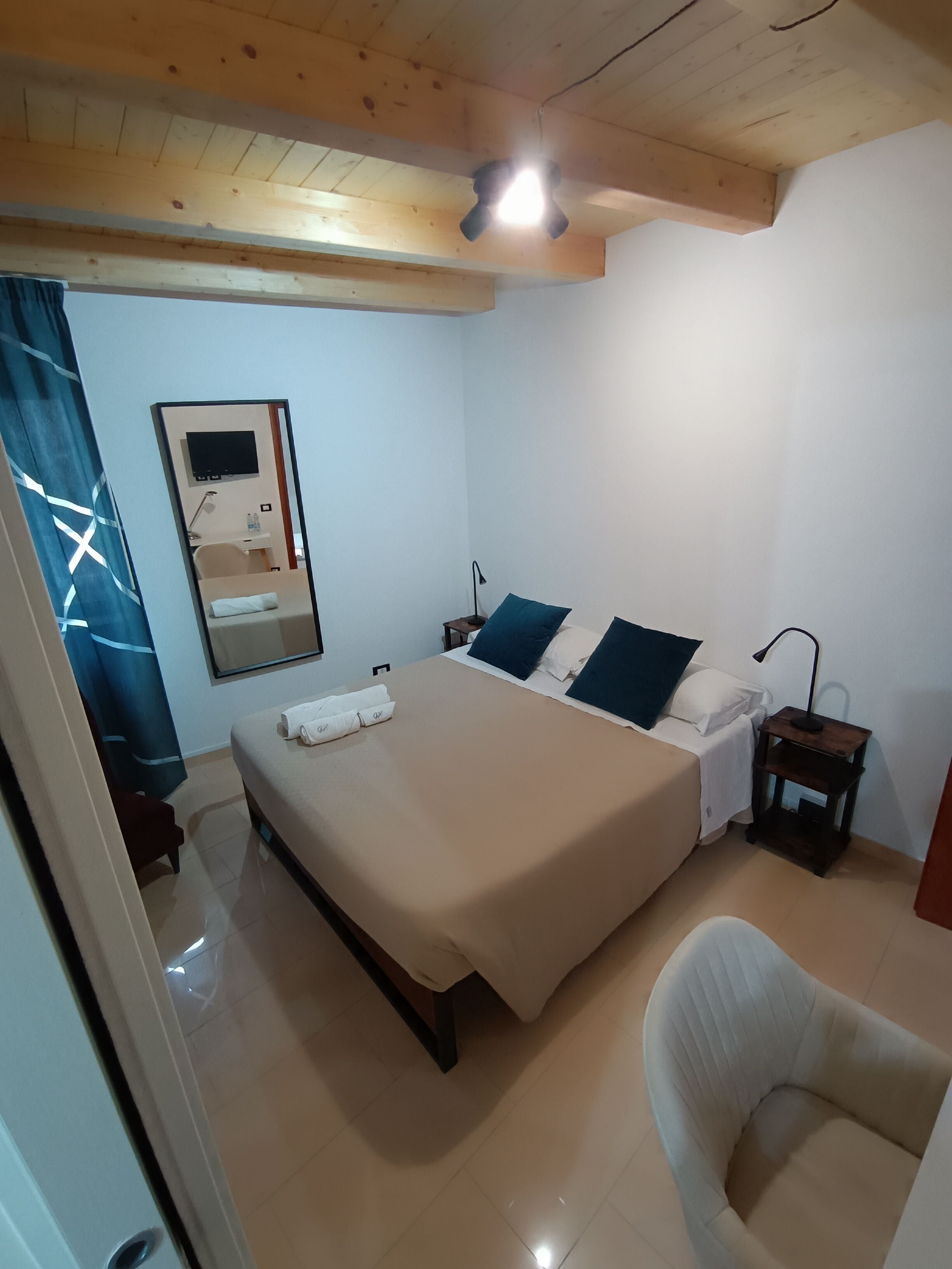 Une chambre à coucher avec un lit, des tables de chevet, une chaise, un miroir et un ventilateur de plafond.