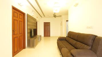 A living room with a brown sofa, wooden doors, a TV on a wooden cabinet, and a ceiling fan.