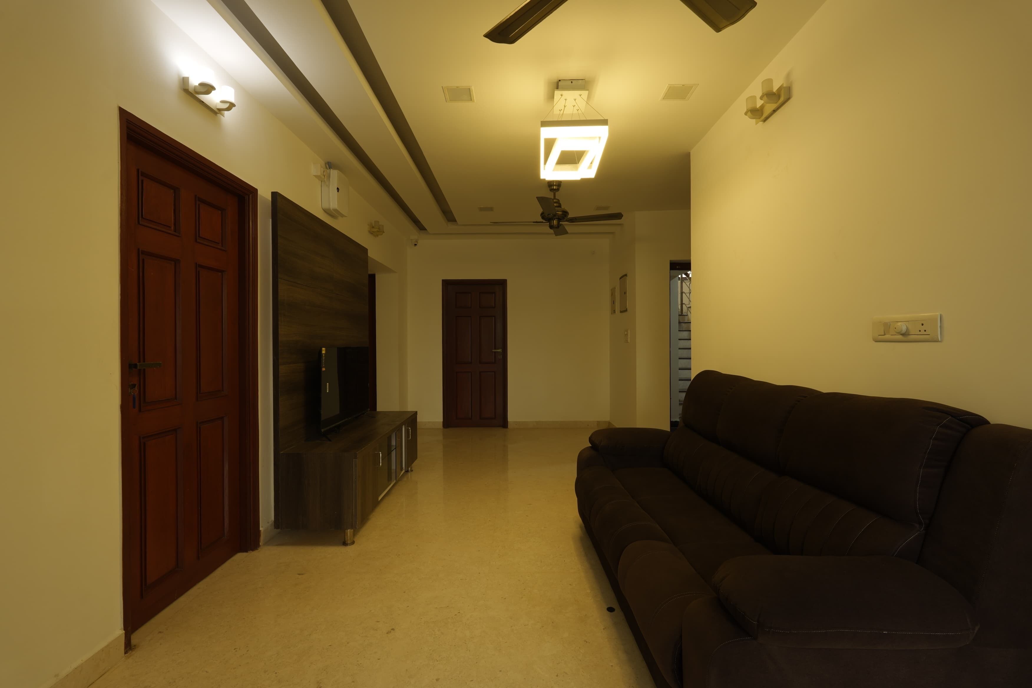 Una sala de estar con un sofá marrón oscuro, un televisor de pantalla plana sobre un mueble de madera y un ventilador de techo.