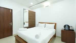 Habitación de hotel con una cama de madera, un espejo grande, un armario y una mesita con una tetera y vasos.