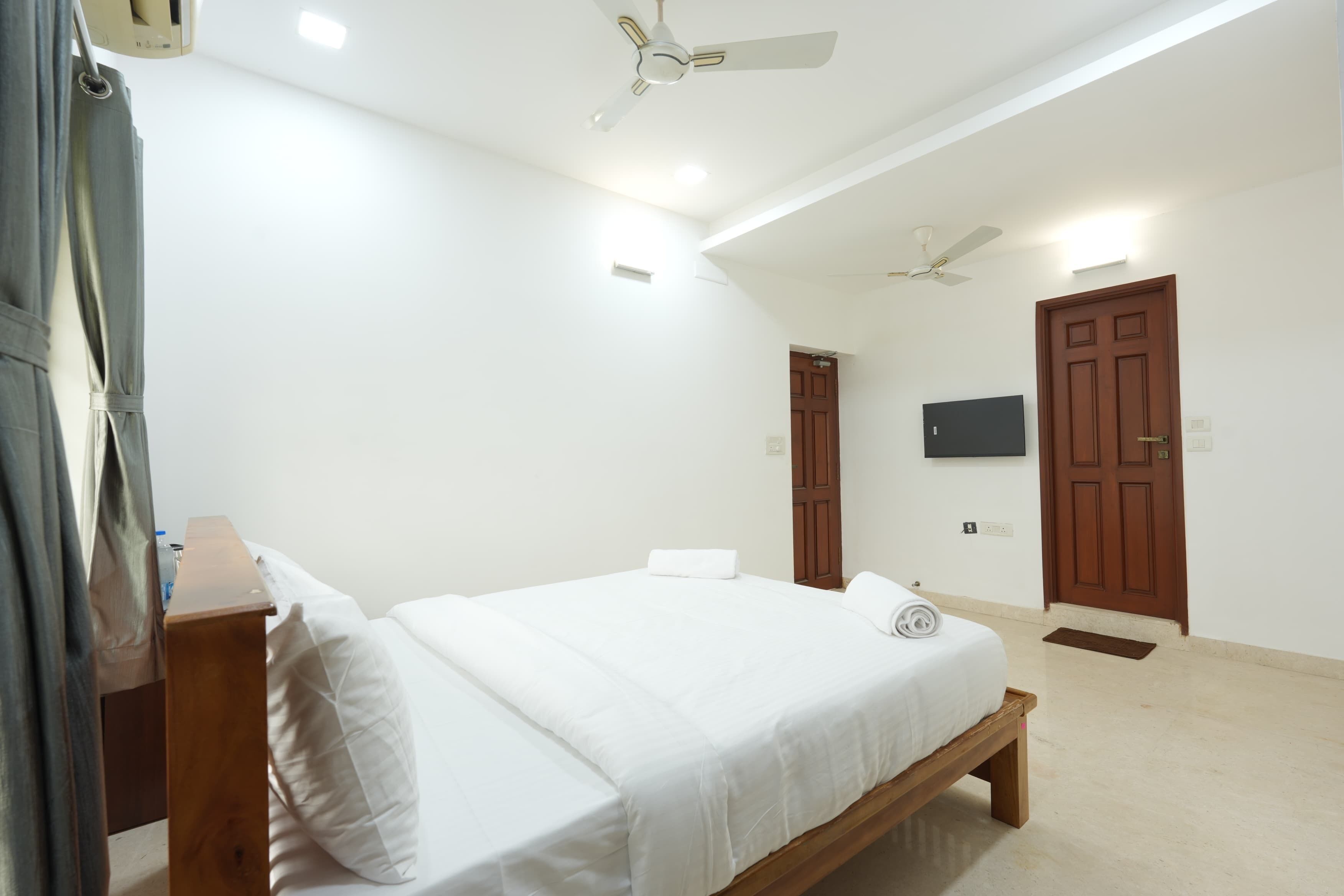 A hotel room with a bed, a wooden bench, a ceiling fan, and a TV mounted on the wall.