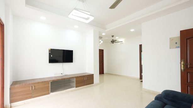 Una sala de estar moderna con un televisor de pantalla plana montado en un mueble de madera, un ventilador de techo, luces empotradas y un sofá azul.