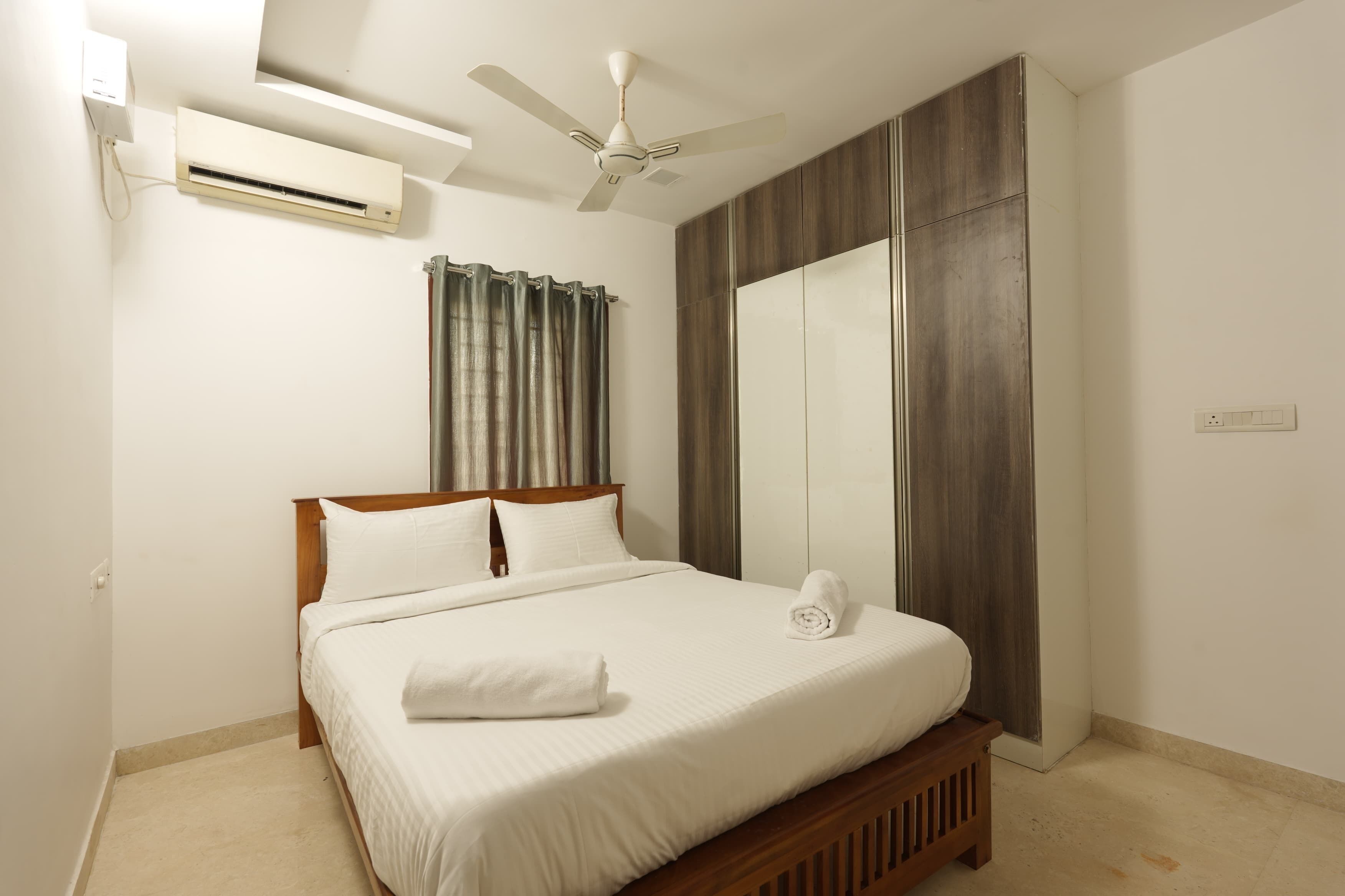 Un dormitorio con cama, ventilador de techo, aire acondicionado, espejo y cortina.