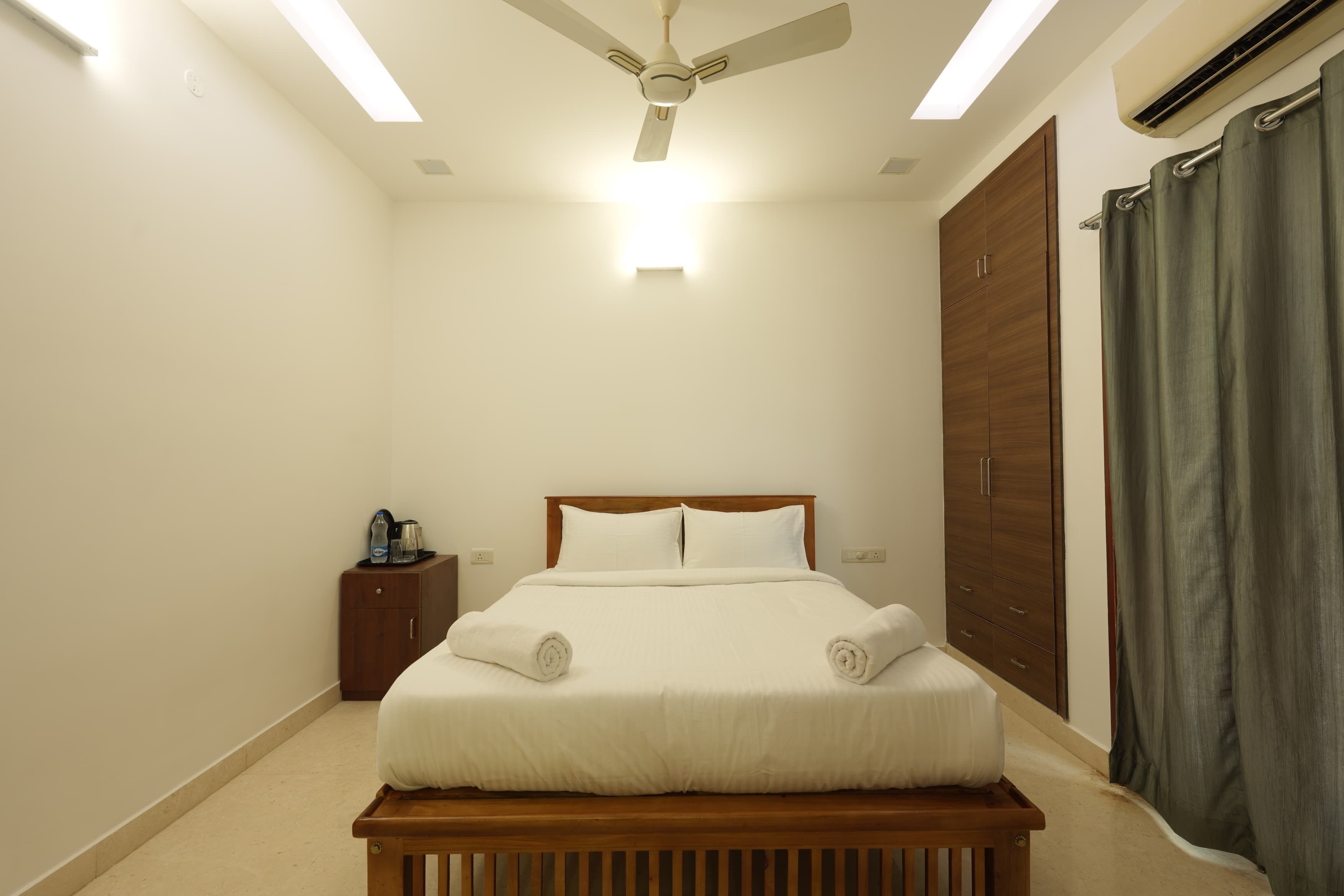A bedroom with a bed, a nightstand, a wardrobe, a ceiling fan, and an air conditioning unit.