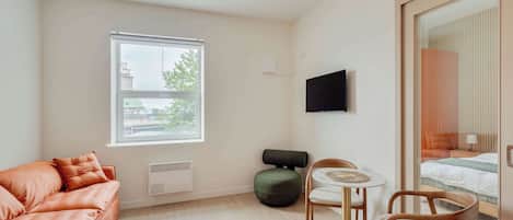 A modern room with a sofa, a small table with chairs, a bed, and a window with blinds.