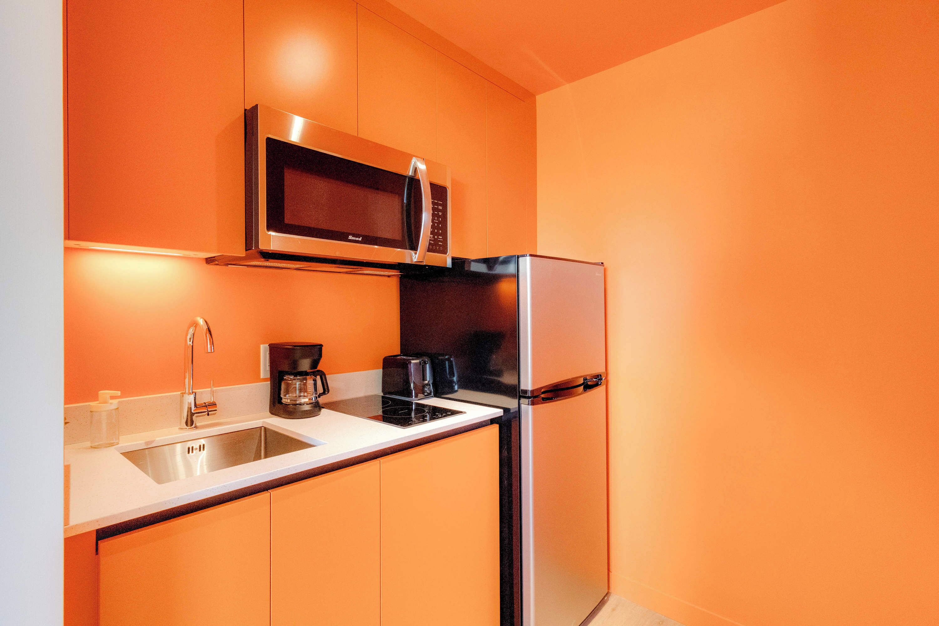A compact kitchen with a microwave, refrigerator, sink, and coffee maker.