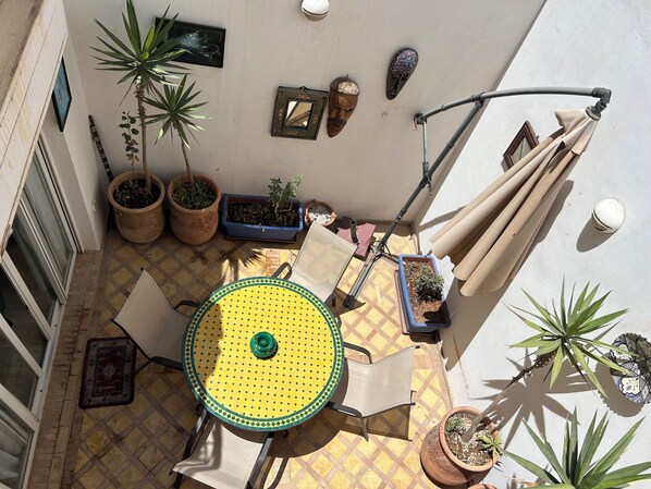 Een terras met een ronde tafel, stoelen, potplanten en een pergola.