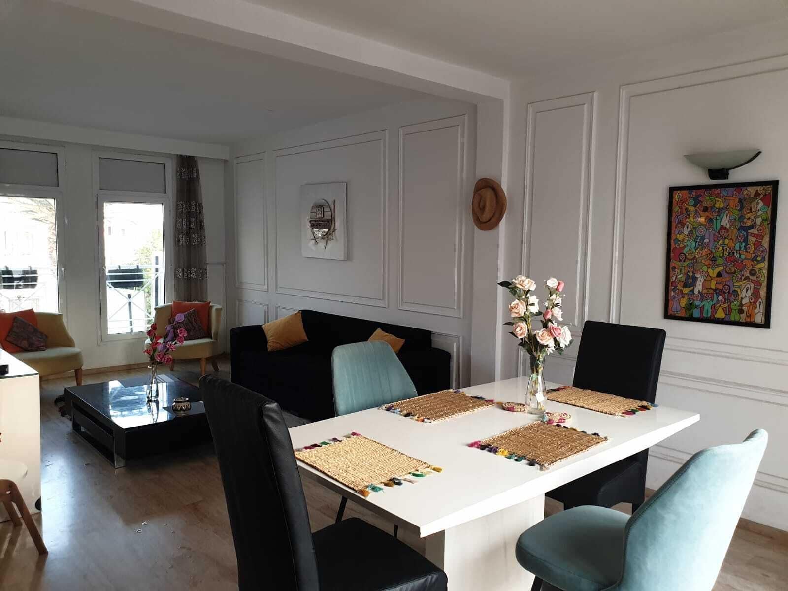 A dining area with a white table, black and teal chairs, and woven placemats.