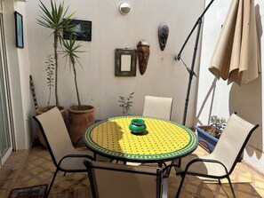 A round table with chairs, potted plants, and wall-mounted decorations in a sunlit outdoor area. - Stylish home for your vacation (Agadir)