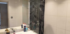 Een badkamer met een douchecabine van glas, een spiegel en toiletartikelen op de wastafel.