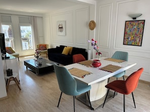 A modern living room with a white dining table, colorful chairs, a black sofa, and a television.
