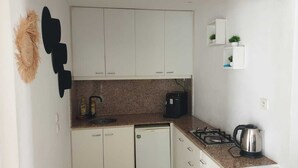 Eine kompakte Küche mit weißen Schränken, einer Granit-Arbeitsplatte, einer Kaffeemaschine, einem Wasserkocher und einem kleinen Regal mit Pflanzen.