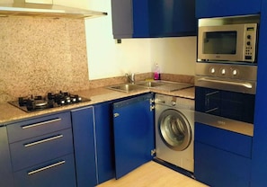 A compact kitchen with a gas stove, a microwave, a washing machine, and a sink.