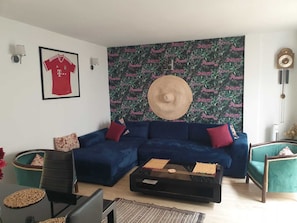 A living room with a blue sofa, a coffee table, and a wall with a tropical print.