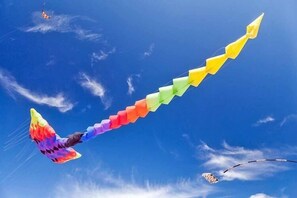 Un cerf-volant aux couleurs vives, orné d’un motif en arc-en-ciel, s’élève dans un ciel bleu dégagé.