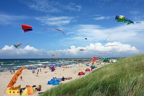 Una playa con tiendas de campaña y gente, con cometas volando en el cielo.