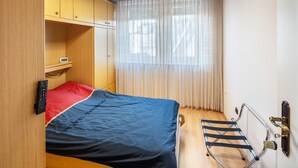 A compact room with a bed, a small shelf, a window with sheer curtains, and a metal rack. - Room 'Einzelzimmer Mit Bad' with Balcony and Wi-Fi (Düsseldorf)