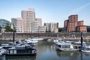 Un port de plaisance où sont amarrés différents types de bateaux, une promenade en bord de mer et, en arrière-plan, des bâtiments modernes.