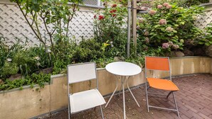 An outdoor seating area with a white round table and two chairs, one white and one orange, positioned on a brick patio. - Room 'Einzelzimmer Mit Bad' with Balcony and Wi-Fi (Düsseldorf)