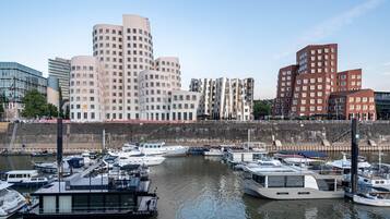 A marina with various boats docked, a waterfront promenade, and modern buildings in the background.