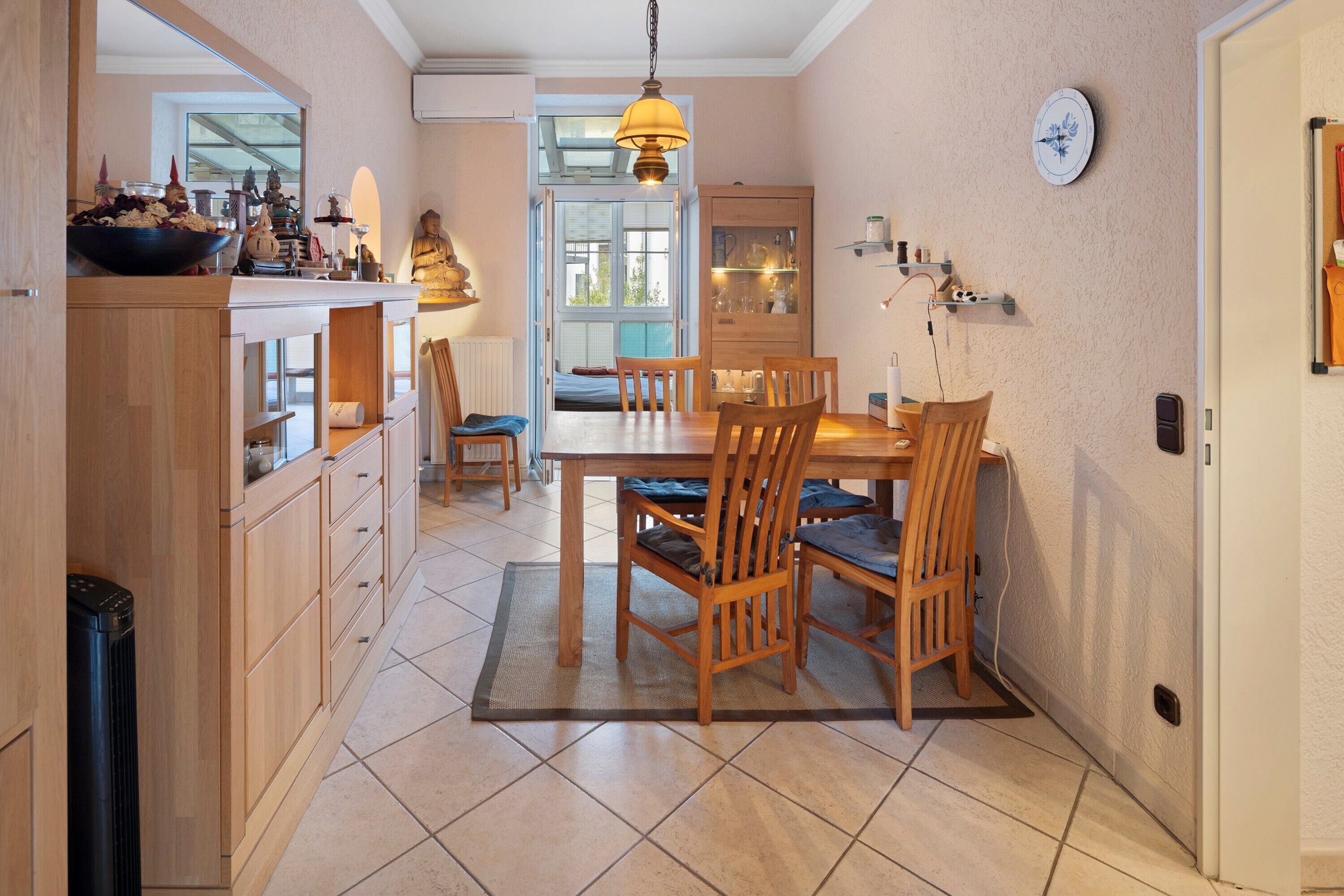 Un coin repas avec une table et des chaises en bois, un luminaire suspendu et une horloge murale.