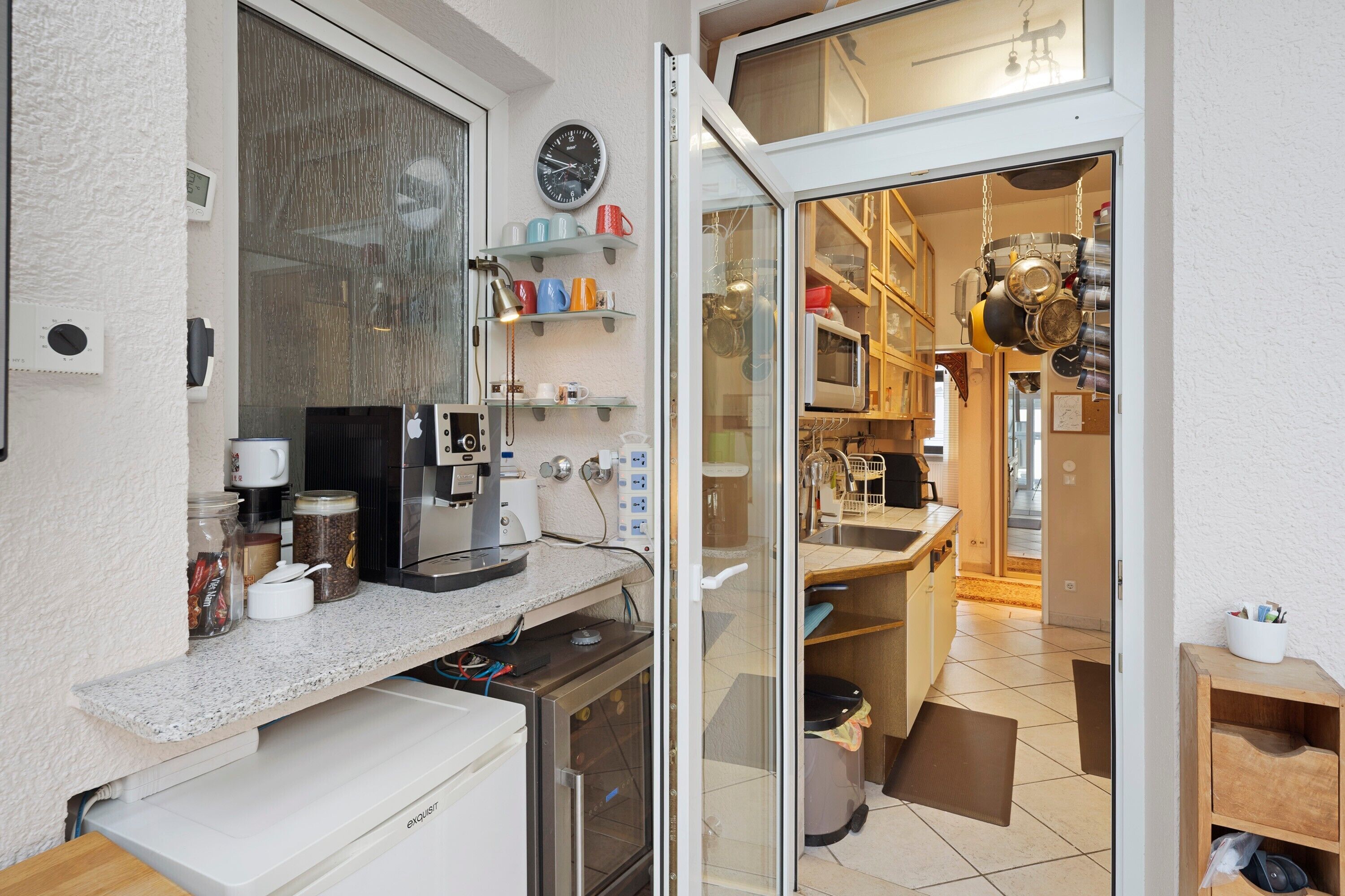 A compact kitchen with a built-in oven, coffee machine, and a small refrigerator.