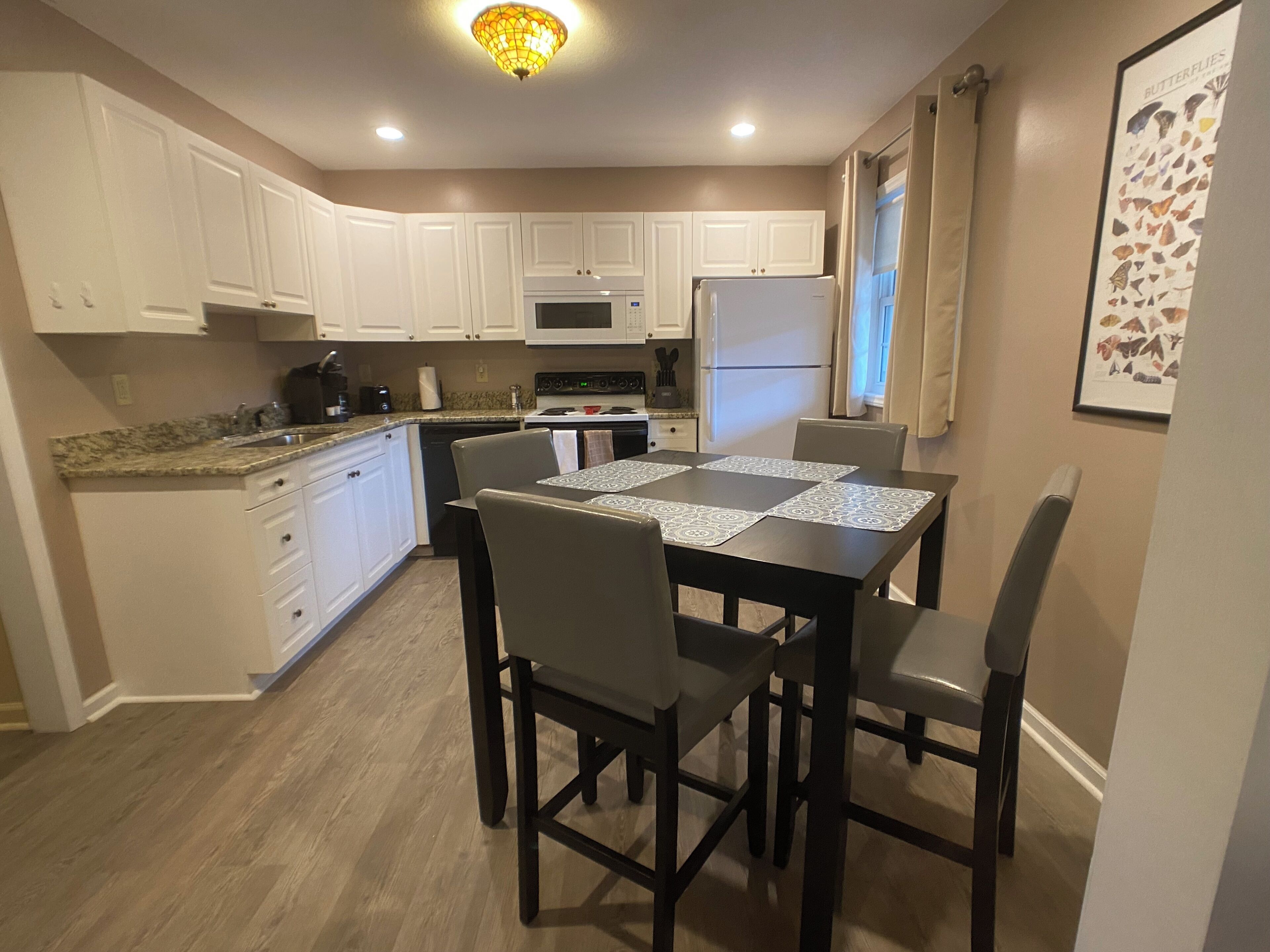 A modern kitchen with white cabinets, a dining table with four chairs, and a refrigerator.
