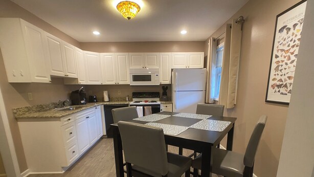 A modern kitchen with white cabinets, a dining table with four chairs, and a refrigerator. - Island Street Loft - downtown convenience with proximity to local attractions! (Bryson City)