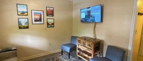 Een woonkamer met een aan de muur bevestigde televisie, een getextureerd vloerkleed, twee fauteuils en een houten dressoir.