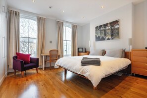 Ein modernes Schlafzimmer mit einem großen Bett, Holzboden, einem Sessel, einem kleinen Tisch und einem Fernseher.