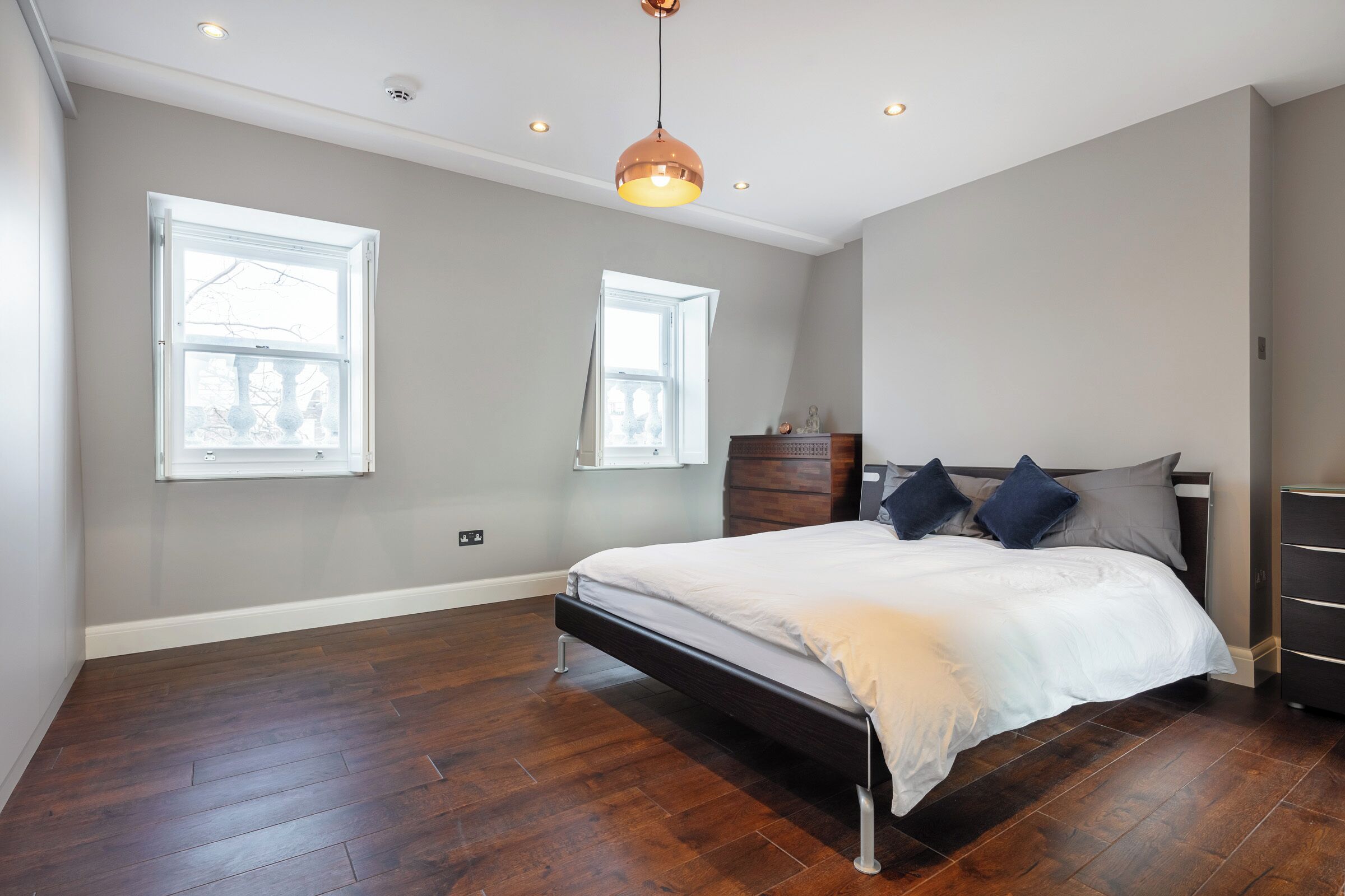 A bedroom with a large bed, two windows, a wooden dresser, and a pendant light.
