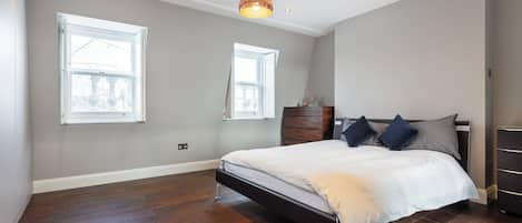 A bedroom with a large bed, two windows, a wooden dresser, and a pendant light.