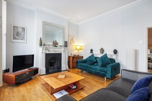 Una sala de estar moderna con un televisor de pantalla plana, una chimenea, un sofá color turquesa y una mesa de centro de madera.