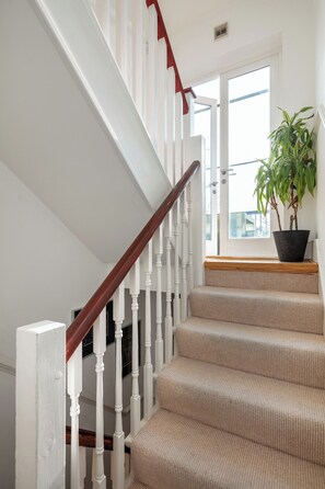 Una escalera con balaustres blancos y barandilla de madera, que conduce a un rellano con una planta en maceta.