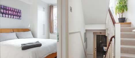 Un dormitorio con una cama, una mesita de noche, una ventana y una escalera que sube a un piso superior.
