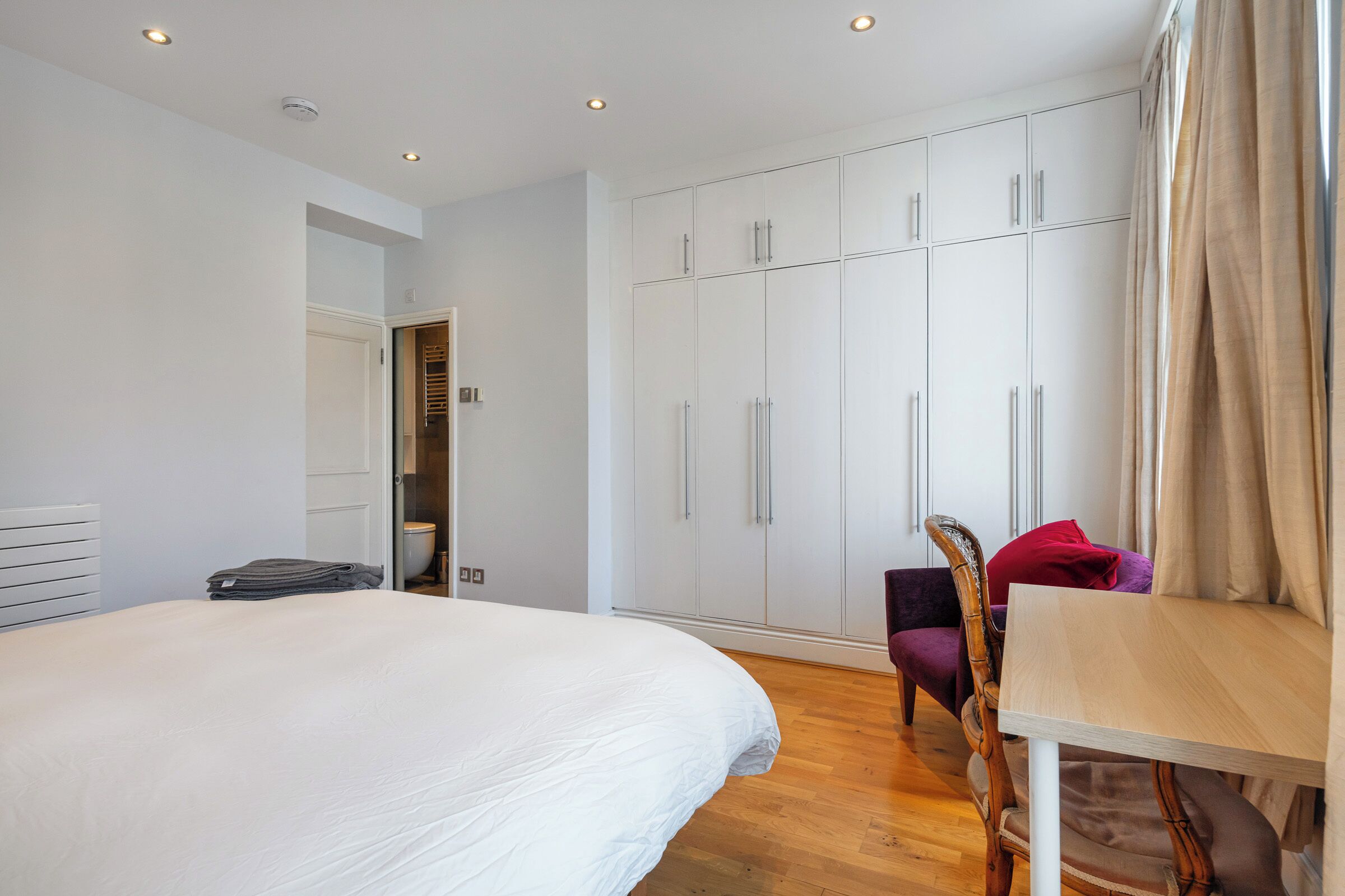 A bedroom with a bed, a wooden table, a chair, and a wardrobe.