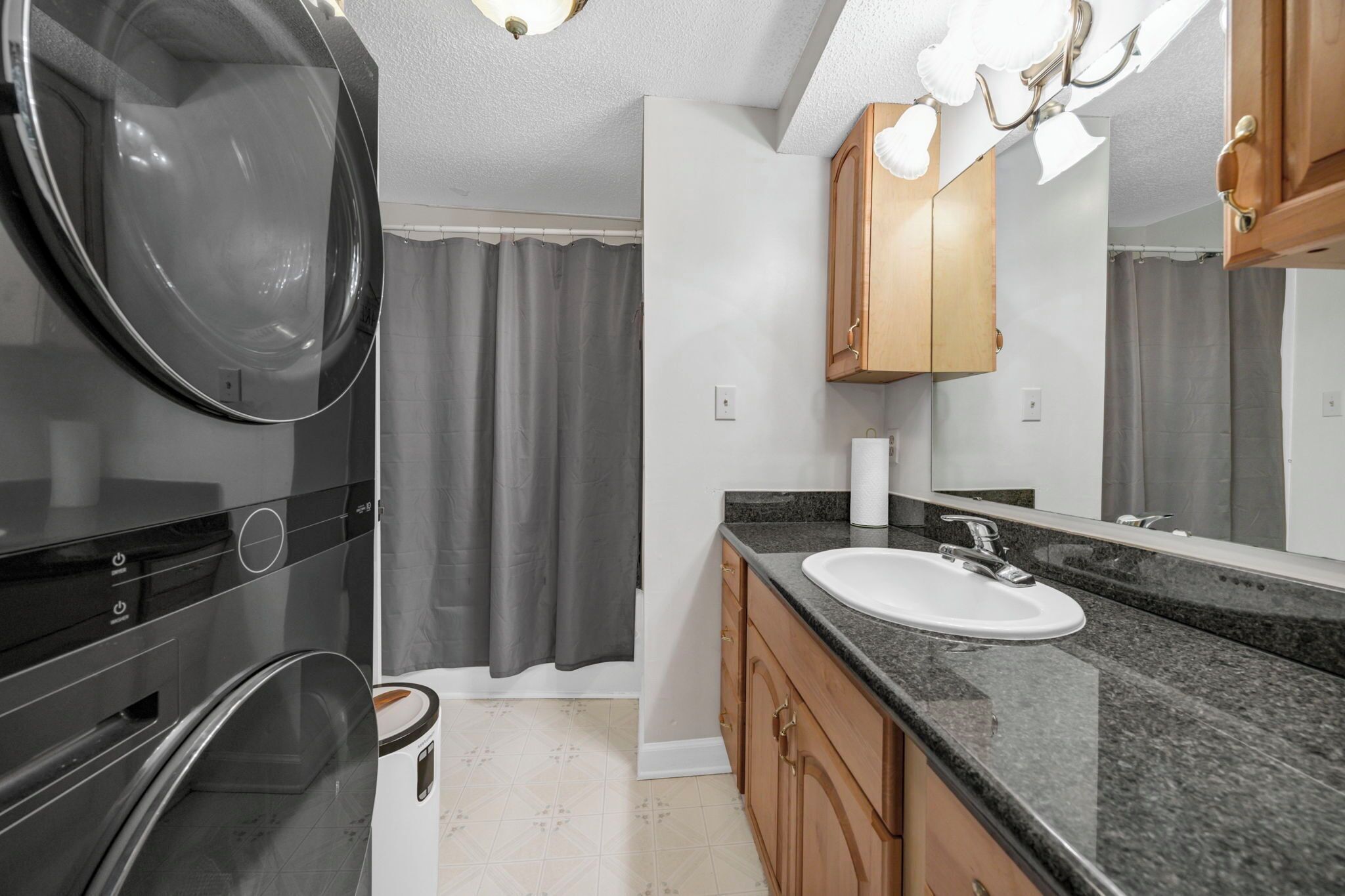 A modern bathroom with a built-in washer, a sink with a mirror, wooden cabinets, and a shower curtain.