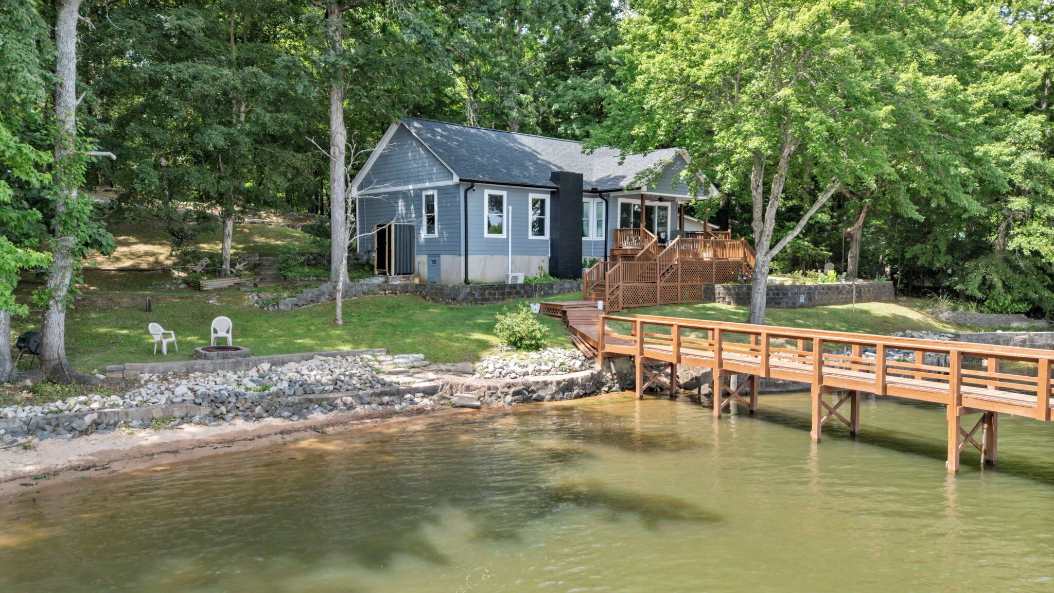 A house with a dock extending over a calm body of water, surrounded by lush greenery.