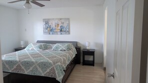 Ein Schlafzimmer mit einem Bett, zwei Nachttischen, einem Deckenventilator, einem Wandbild und einer Tür.