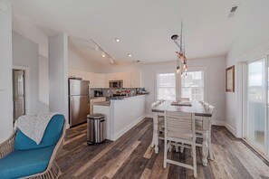 A modern kitchen with a central island, stainless steel appliances, and a dining area with a rustic table and chairs. - JL #061 E Z Livin - Hot Tub - Close to beach (Kill Devil Hills)