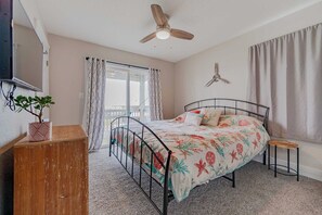 A bedroom with a bed, a ceiling fan, a window with curtains, a small stool, and a plant. - JL #061 E Z Livin - Hot Tub - Close to beach (Kill Devil Hills)