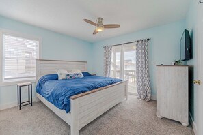 Une chambre à coucher avec un lit, un ventilateur de plafond, une fenêtre avec des stores, une porte et un téléviseur fixé au mur.