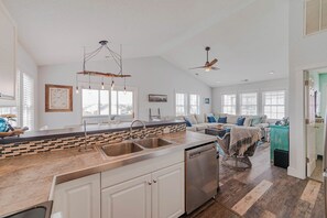 A spacious kitchen with a large island, a dining area with a sofa, and a living room with a fireplace. - JL #061 E Z Livin - Hot Tub - Close to beach (Kill Devil Hills)