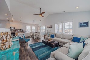 A spacious living area with a sofa, coffee table, and a dining table. - JL #061 E Z Livin - Hot Tub - Close to beach (Kill Devil Hills)
