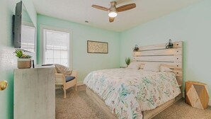 Ein Schlafzimmer mit Bett, Schreibtisch, Stuhl, Deckenventilator und Fenster.