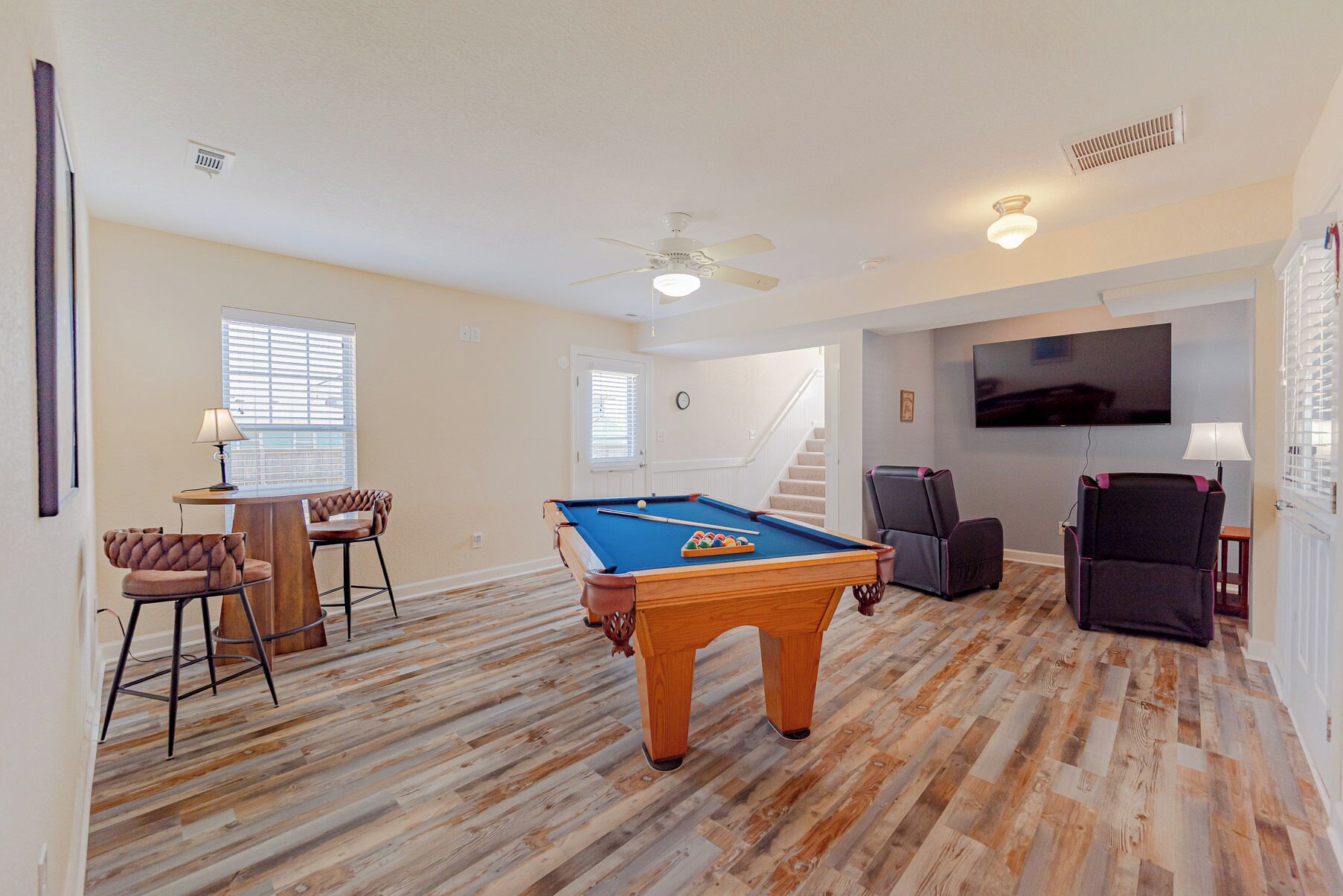 Une pièce équipée d’une table de billard, d’un ventilateur de plafond, d’un téléviseur et d’un escalier.